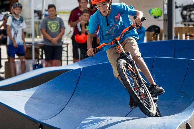 Jugendlicher fährt mit Mountainbike auf einem blauen Pumptrack