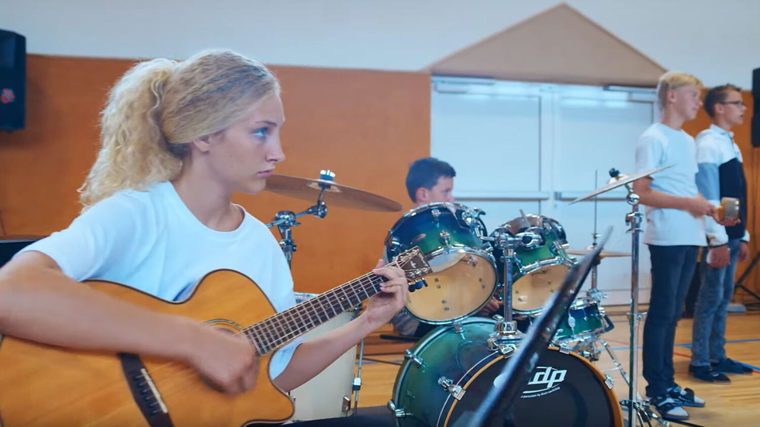 Schülerin spielt auf einer Gitarre. Im Hintergrund ein Schlagzeug.